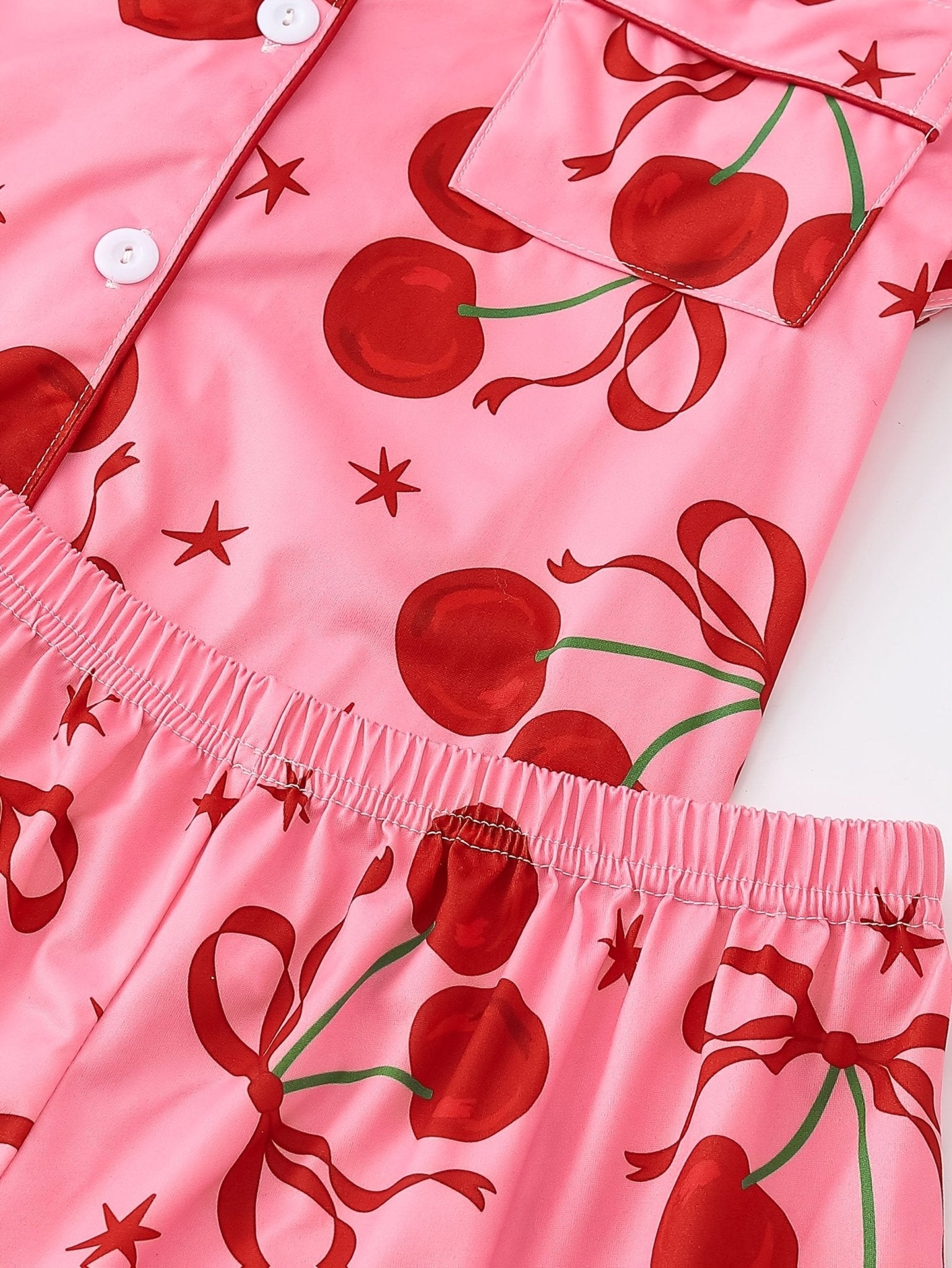 Pink satin-look short-sleeve pajama set with red cherry and bow print, piped trim, chest pocket and elastic waist shorts in 95% Polyester 5% Elastane
