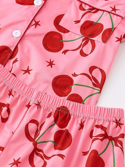 Pink satin-look short-sleeve pajama set with red cherry and bow print, piped trim, chest pocket and elastic waist shorts in 95% Polyester 5% Elastane