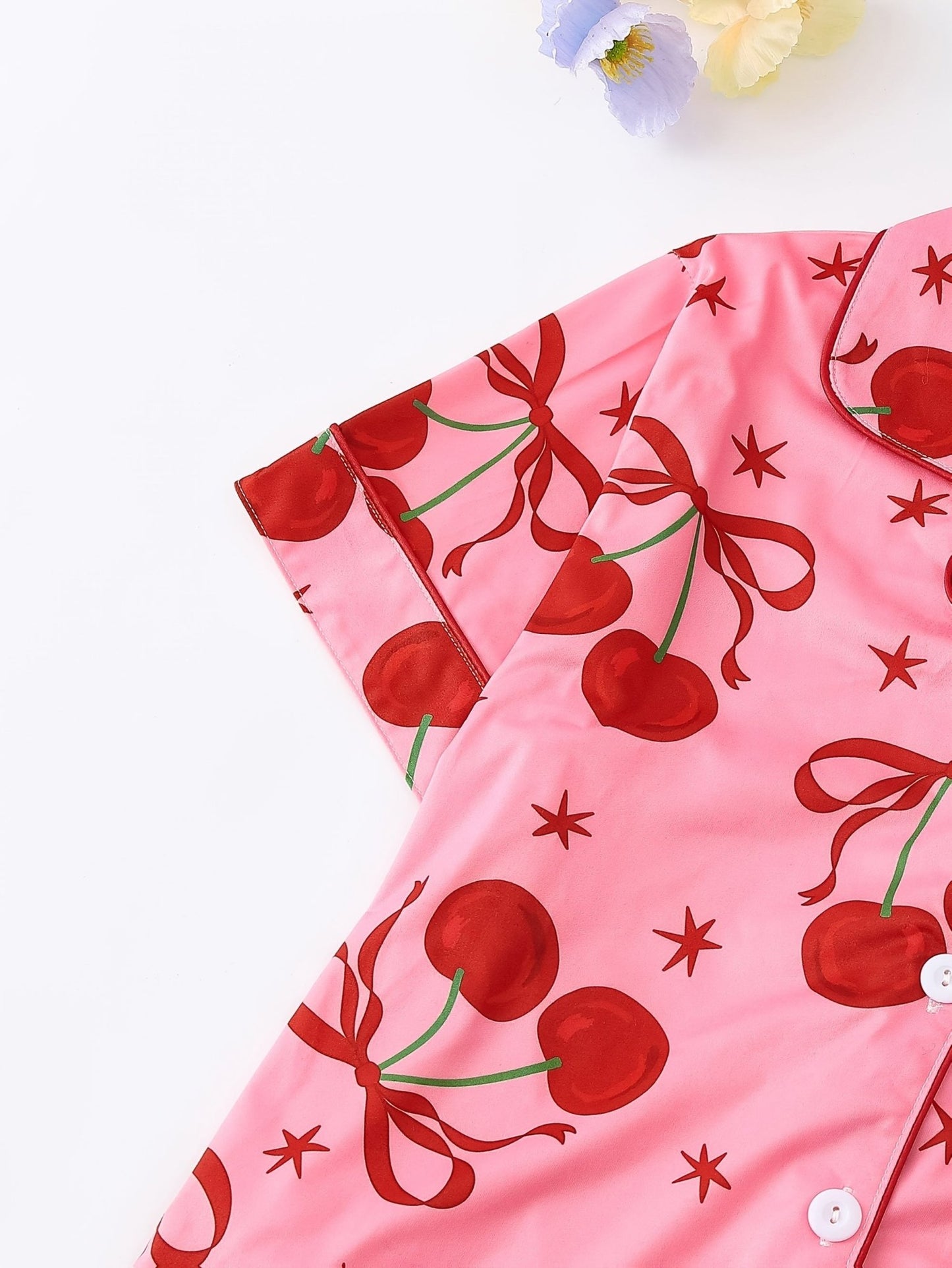 Pink satin-look short-sleeve pajama set with red cherry and bow print, piped trim, chest pocket and elastic waist shorts in 95% Polyester 5% Elastane
