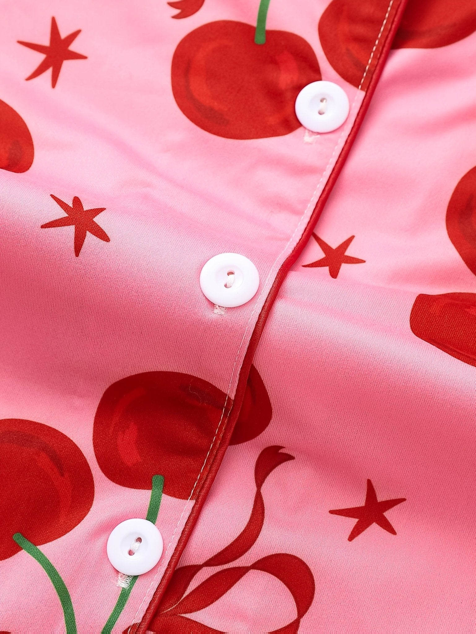 Pink satin-look short-sleeve pajama set with red cherry and bow print, piped trim, chest pocket and elastic waist shorts in 95% Polyester 5% Elastane