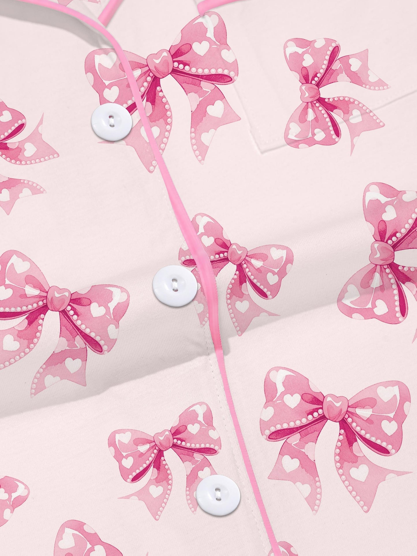 Pastel pink short-sleeve pajama set with heart-dotted bow print — button-up top and elastic waist shorts with pink piping
