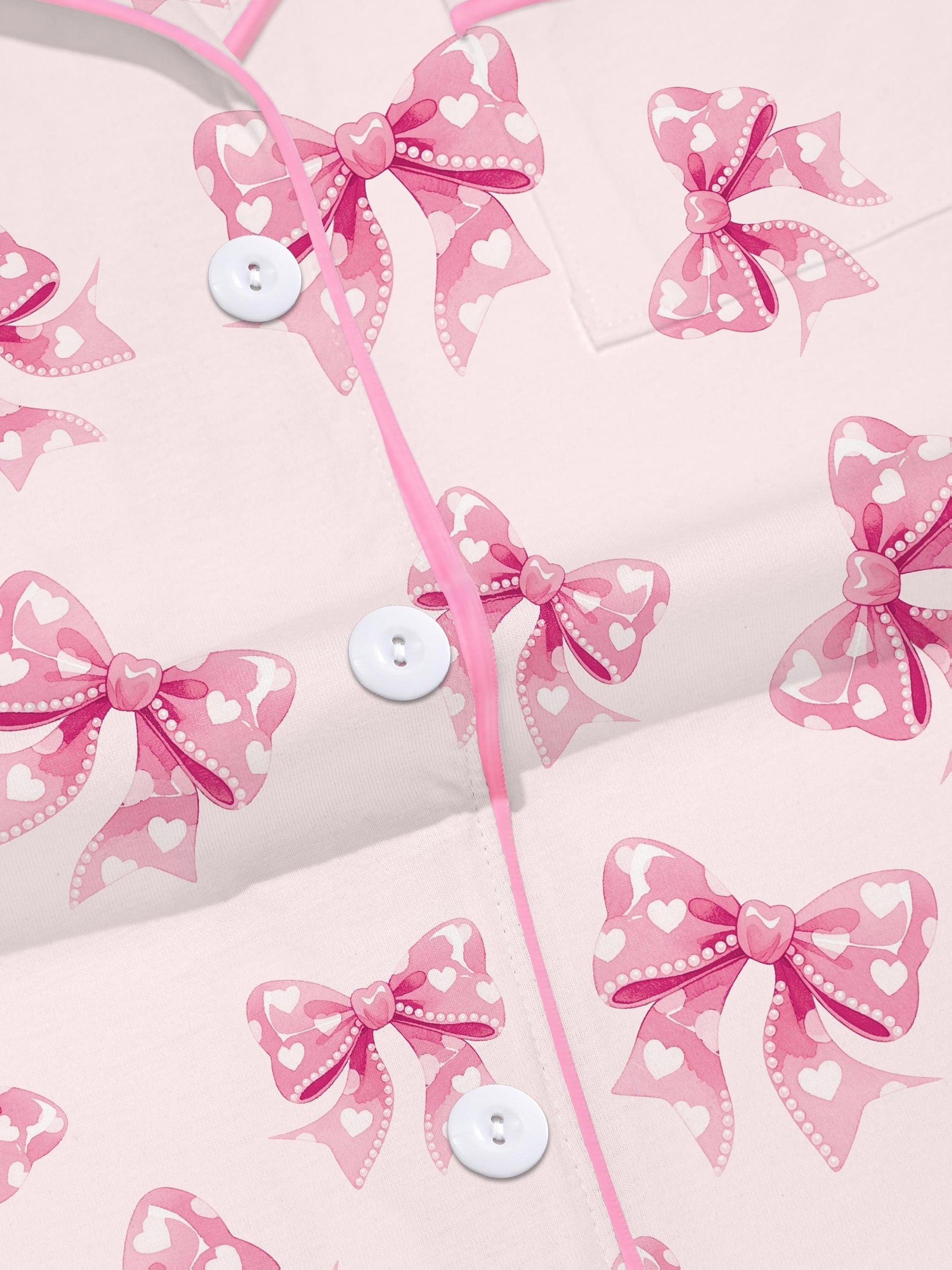 Pastel pink short-sleeve pajama set with heart-dotted bow print — button-up top and elastic waist shorts with pink piping