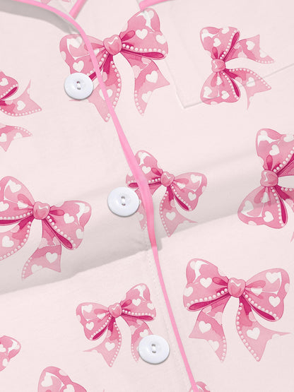 Pastel pink short-sleeve pajama set with heart-dotted bow print — button-up top and elastic waist shorts with pink piping