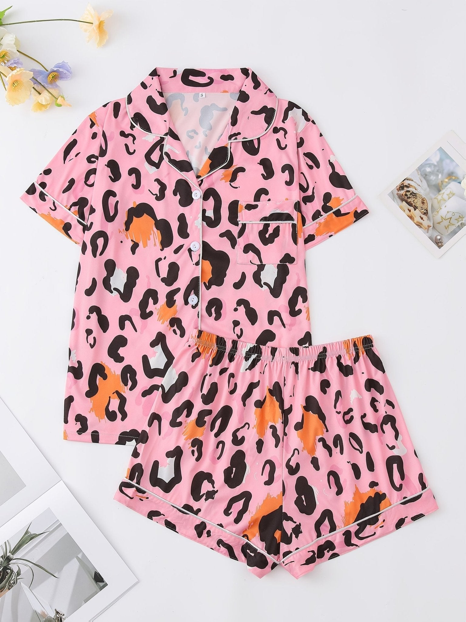 Pink satin-look short-sleeve pajama set with black and orange leopard print, piped trim, chest pocket and elastic waist shorts in 95% Polyester 5% Elastane — silky stretch travel-ready loungewear