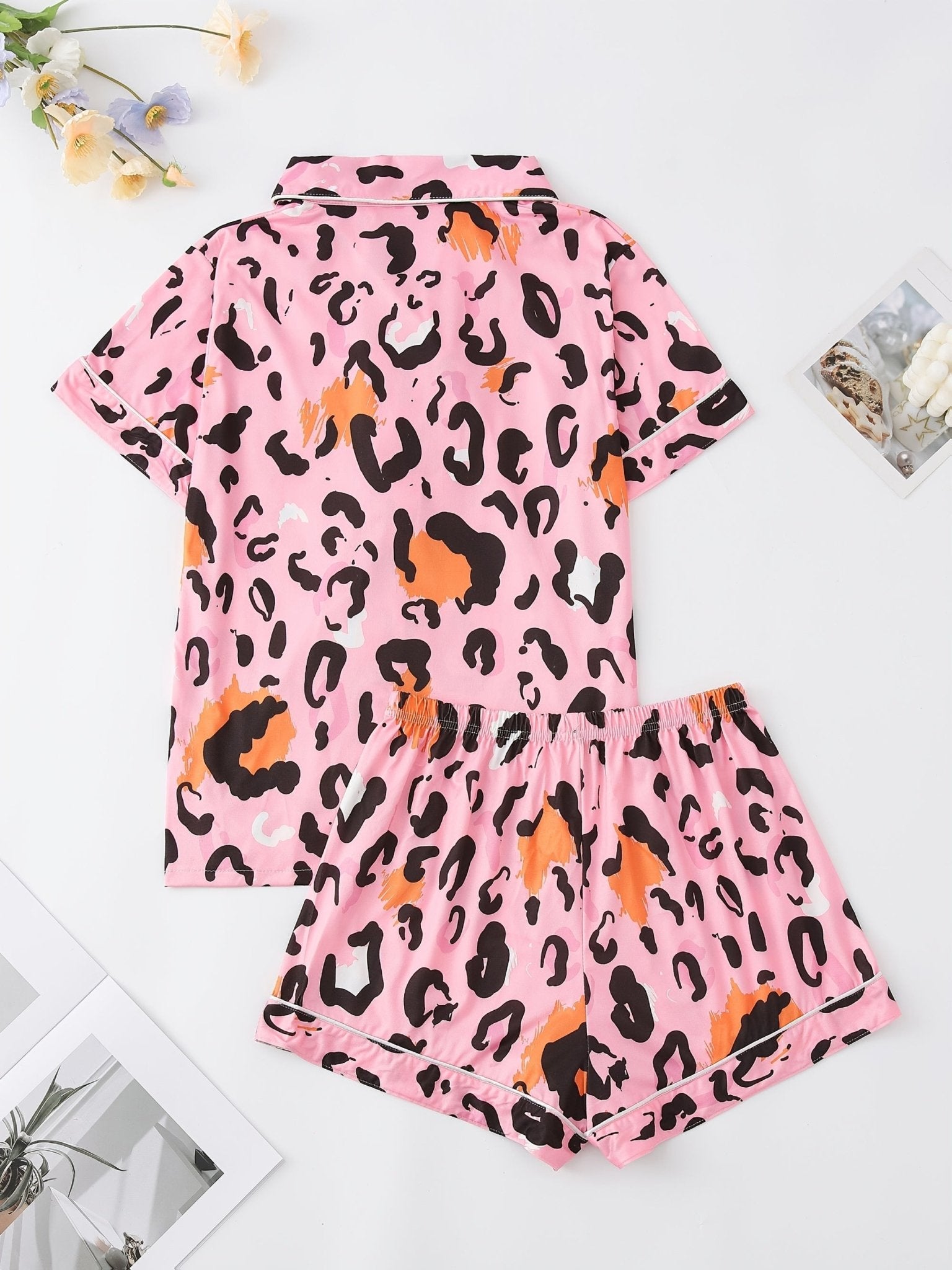 Pink satin-look short-sleeve pajama set with black and orange leopard print, piped trim, chest pocket and elastic waist shorts in 95% Polyester 5% Elastane — silky stretch travel-ready loungewear
