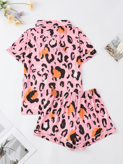 Pink satin-look short-sleeve pajama set with black and orange leopard print, piped trim, chest pocket and elastic waist shorts in 95% Polyester 5% Elastane — silky stretch travel-ready loungewear