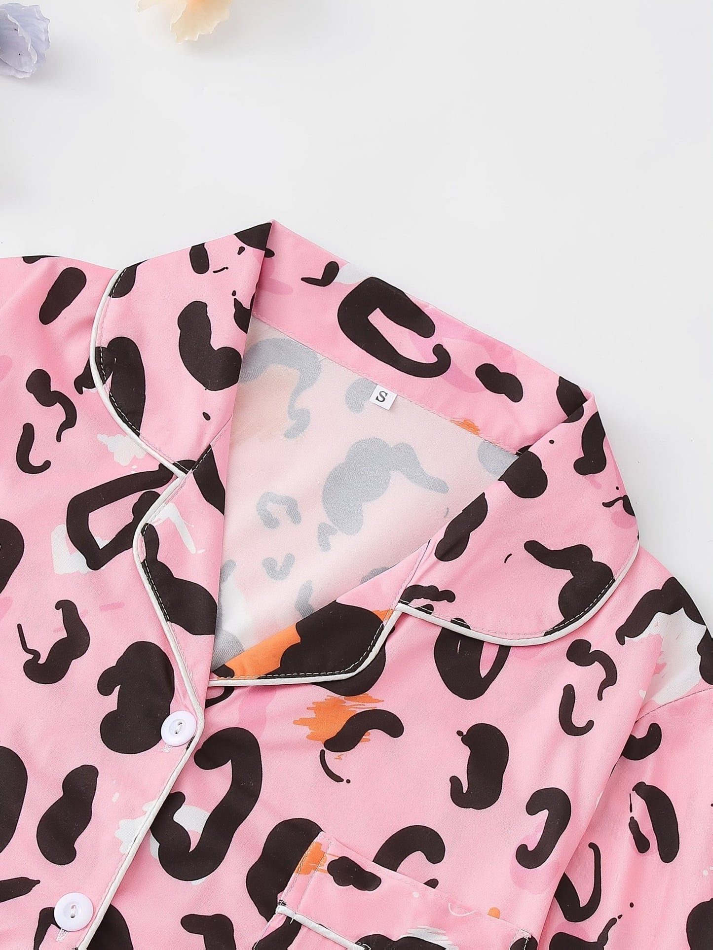 Pink satin-look short-sleeve pajama set with black and orange leopard print, piped trim, chest pocket and elastic waist shorts in 95% Polyester 5% Elastane — silky stretch travel-ready loungewear