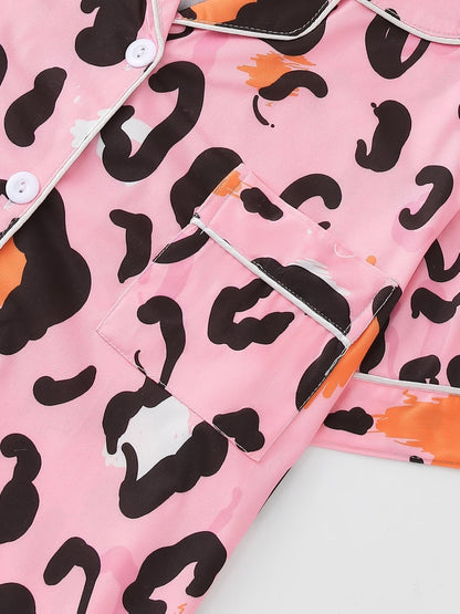 Pink satin-look short-sleeve pajama set with black and orange leopard print, piped trim, chest pocket and elastic waist shorts in 95% Polyester 5% Elastane — silky stretch travel-ready loungewear