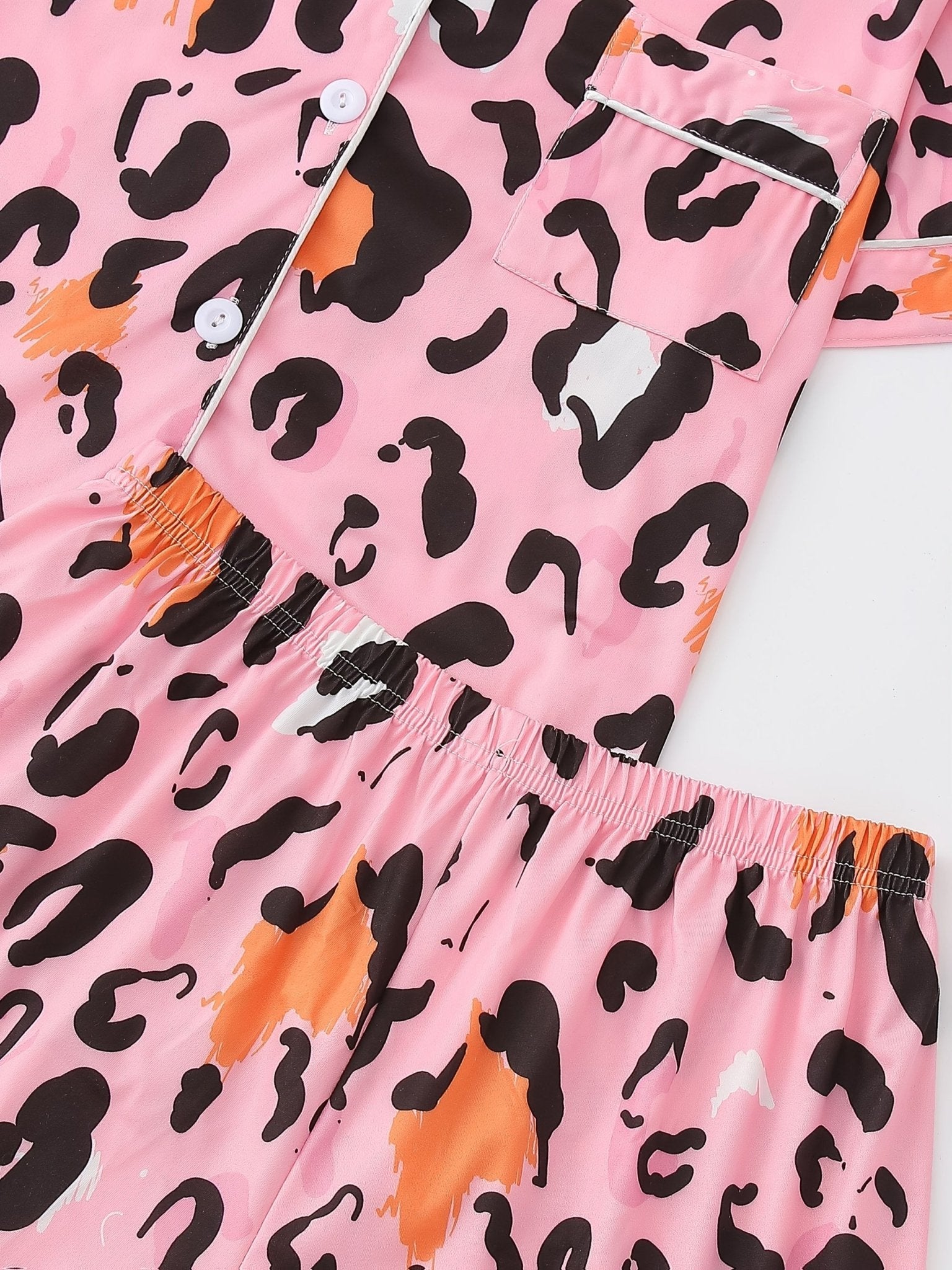 Pink satin-look short-sleeve pajama set with black and orange leopard print, piped trim, chest pocket and elastic waist shorts in 95% Polyester 5% Elastane — silky stretch travel-ready loungewear