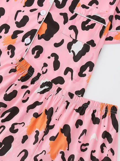 Pink satin-look short-sleeve pajama set with black and orange leopard print, piped trim, chest pocket and elastic waist shorts in 95% Polyester 5% Elastane — silky stretch travel-ready loungewear