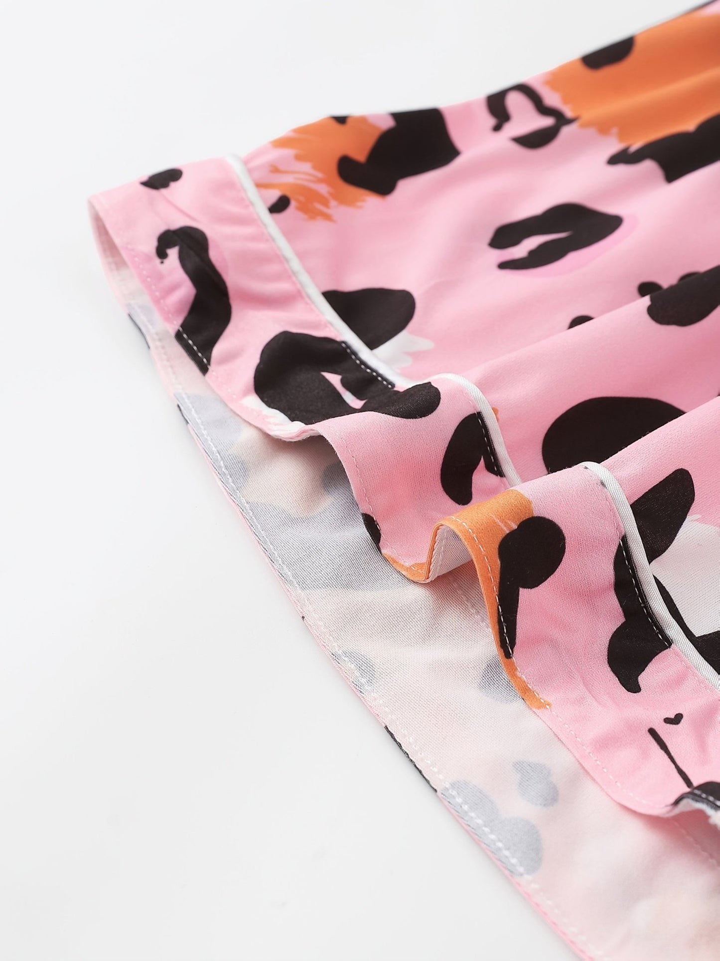 Pink satin-look short-sleeve pajama set with black and orange leopard print, piped trim, chest pocket and elastic waist shorts in 95% Polyester 5% Elastane — silky stretch travel-ready loungewear