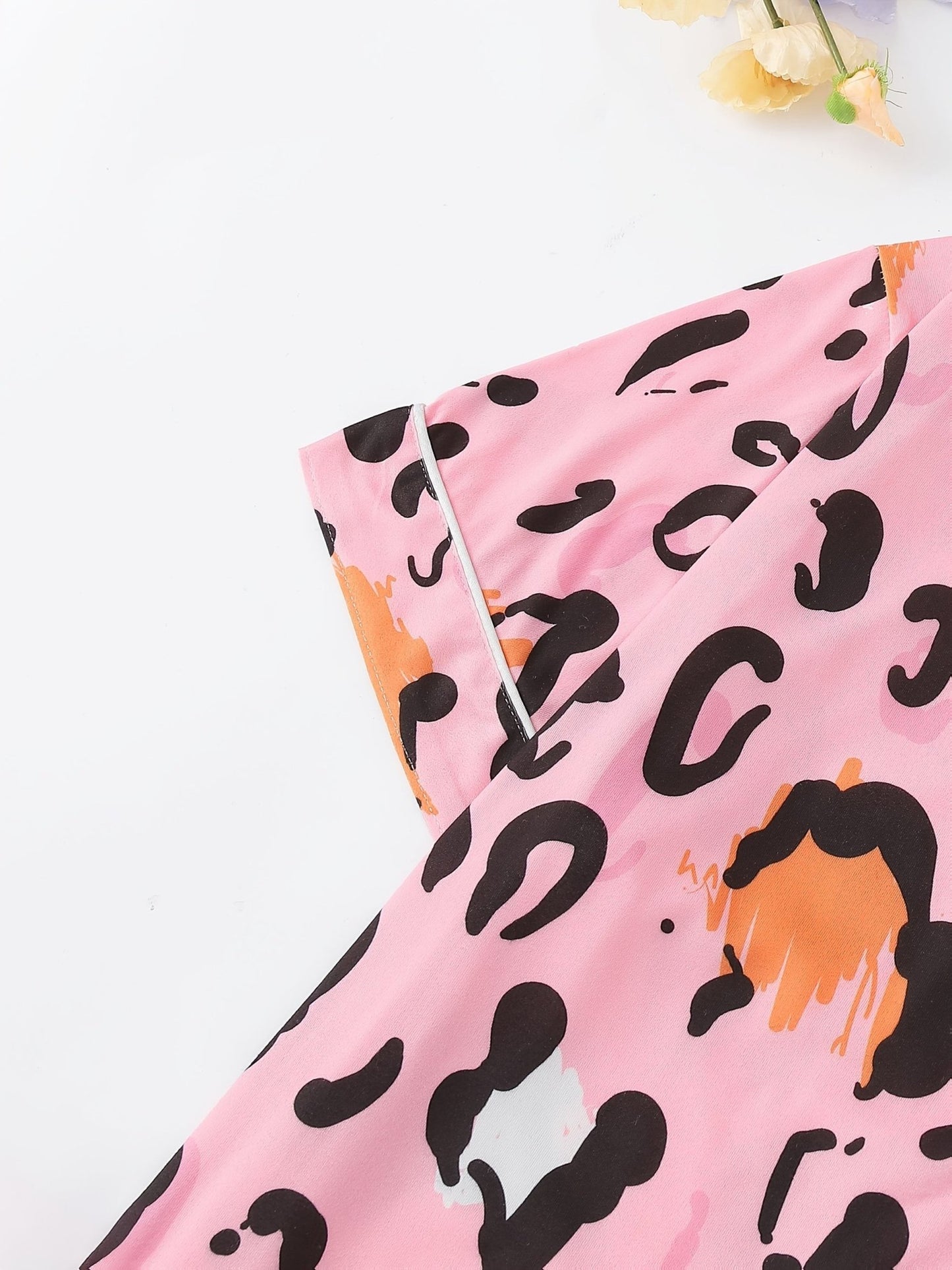 Pink satin-look short-sleeve pajama set with black and orange leopard print, piped trim, chest pocket and elastic waist shorts in 95% Polyester 5% Elastane — silky stretch travel-ready loungewear
