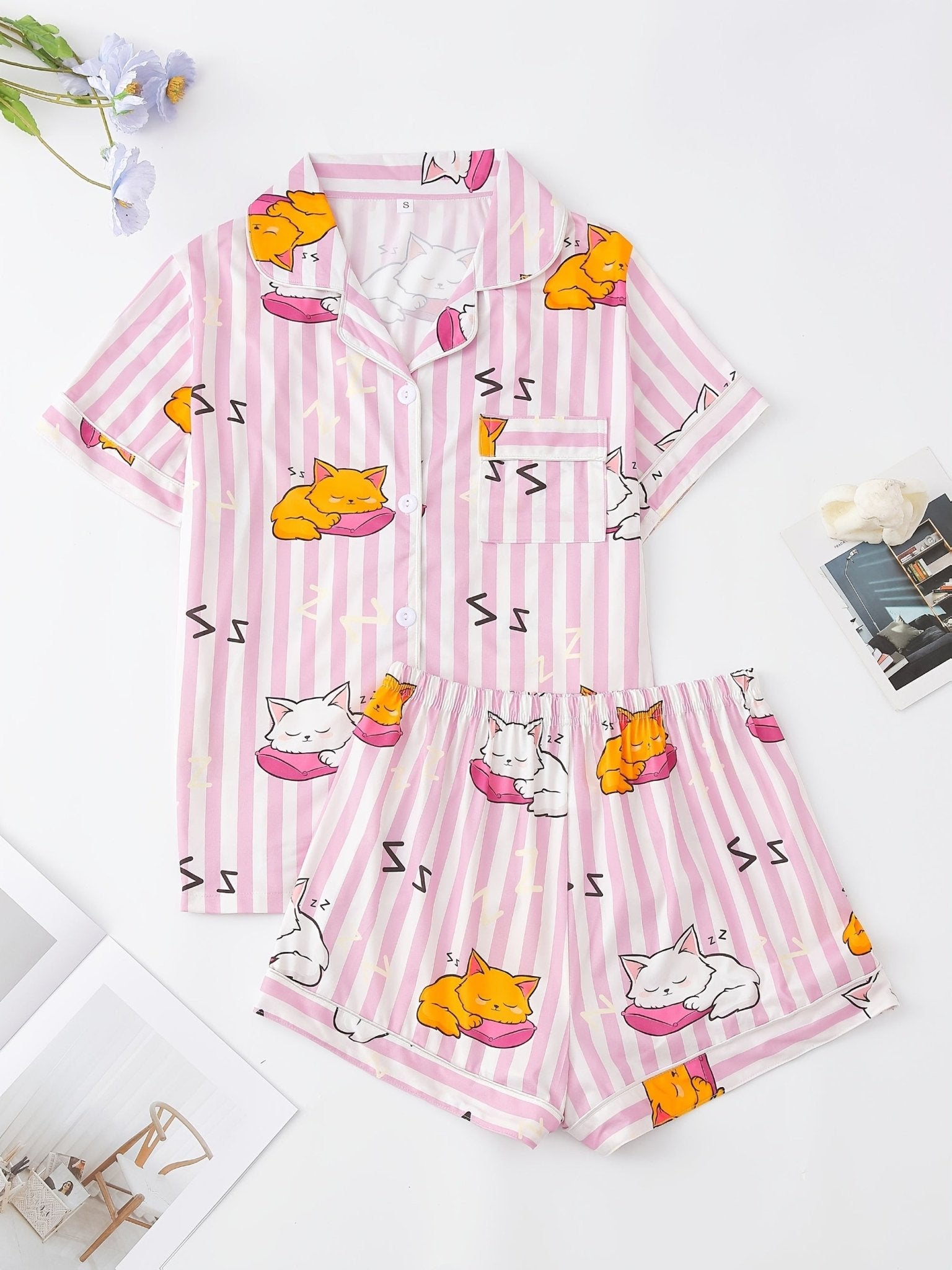 Pink stripe satin-look short-sleeve pajama set with orange and white sleeping cat print, piped trim, chest pocket and elastic waist shorts in 95% Polyester 5% Elastane — silky stretch travel-ready loungewear
