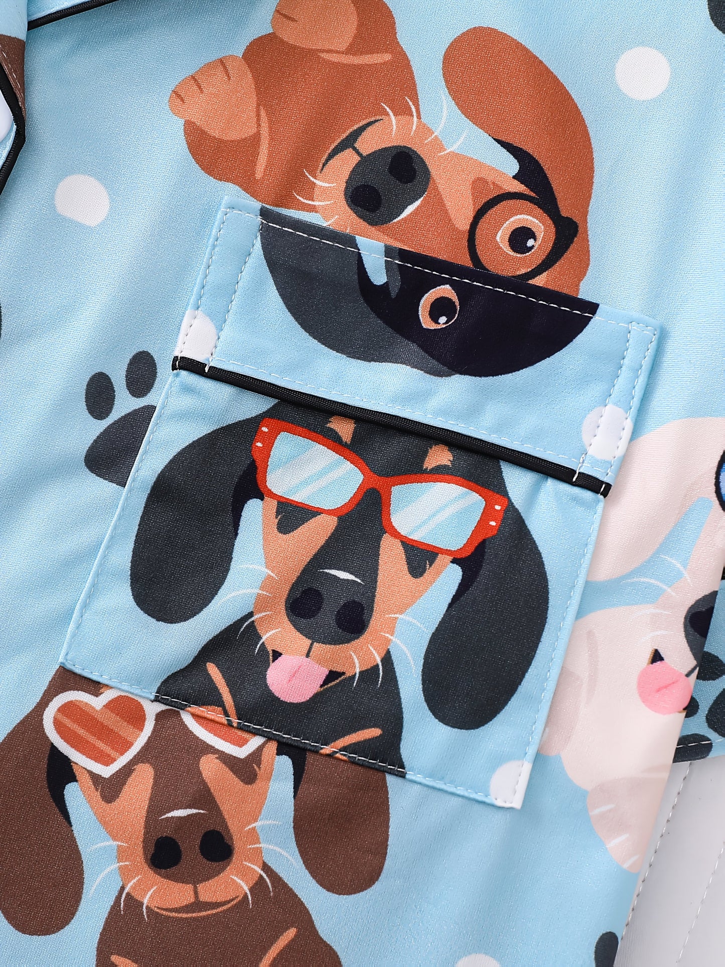 Sky-blue satin-look pajama set with playful dachshund and paw-print pattern — short-sleeve button-up top with chest pocket and elastic waist shorts, 95% Polyester/5% Elastane