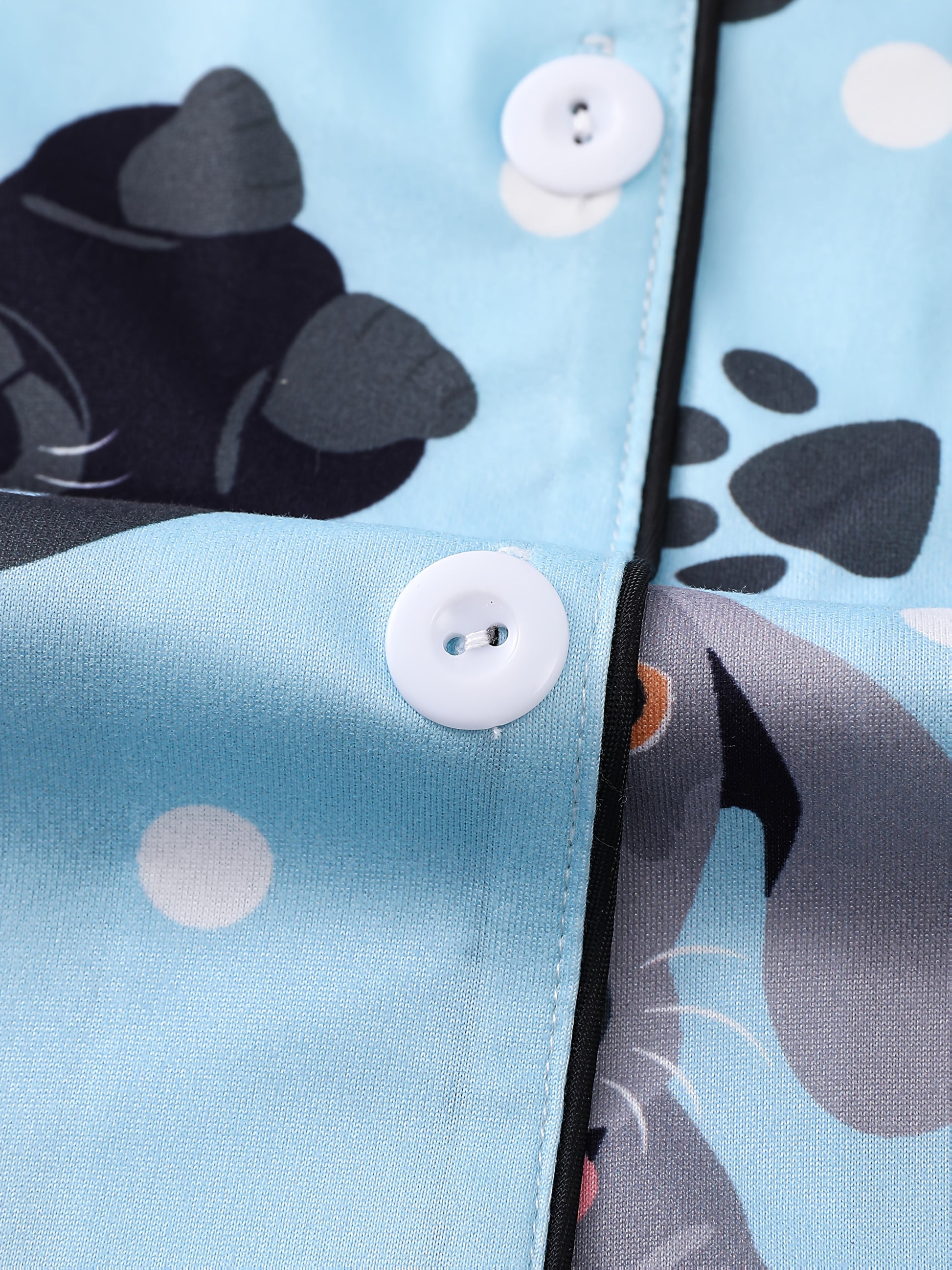 Sky-blue satin-look pajama set with playful dachshund and paw-print pattern — short-sleeve button-up top with chest pocket and elastic waist shorts, 95% Polyester/5% Elastane