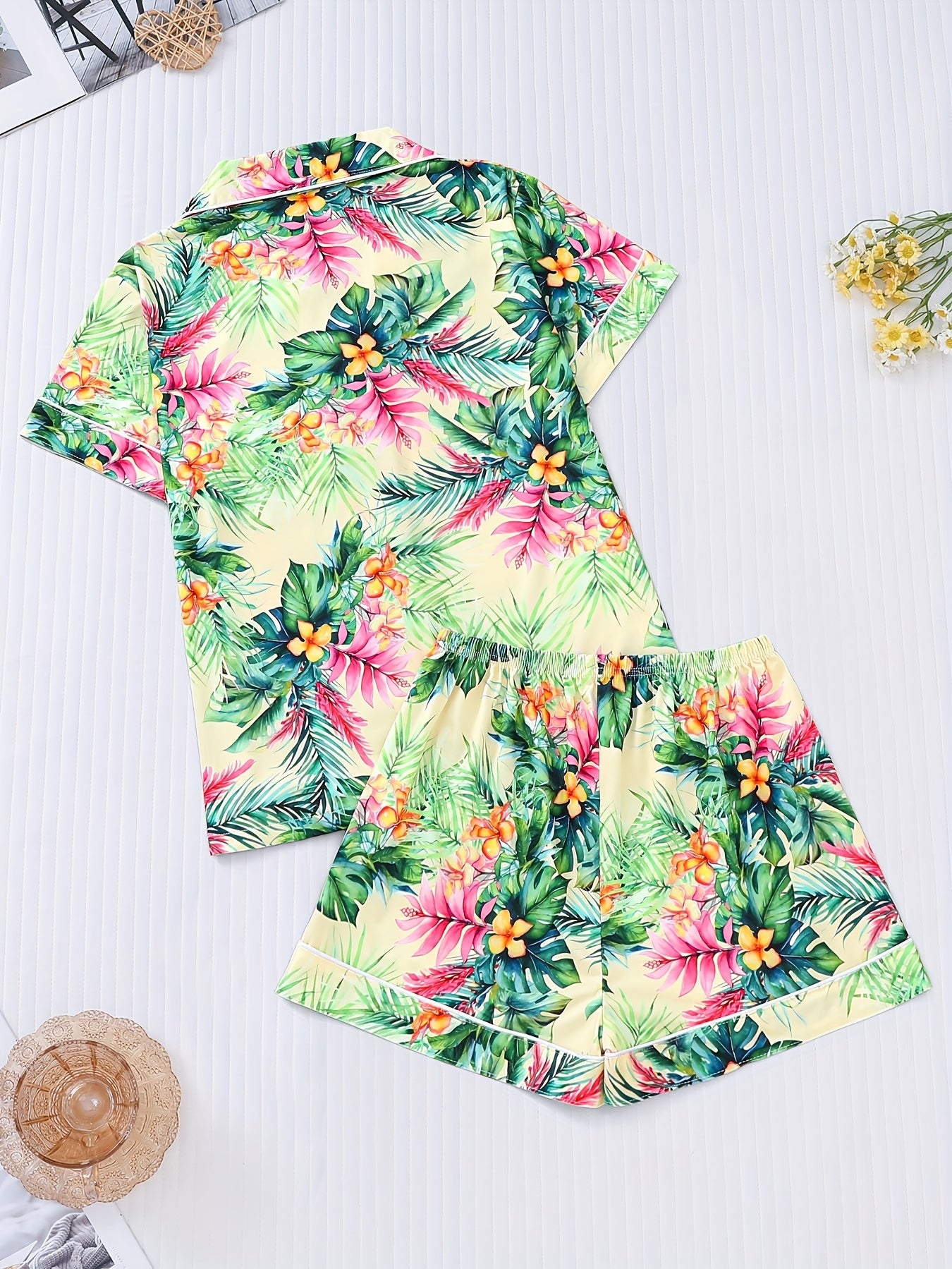 Cream satin-look pajama set with vibrant tropical floral and palm leaf print — short-sleeve button-up top with chest pocket and elastic waist shorts, 95% Polyester/5% Elastane