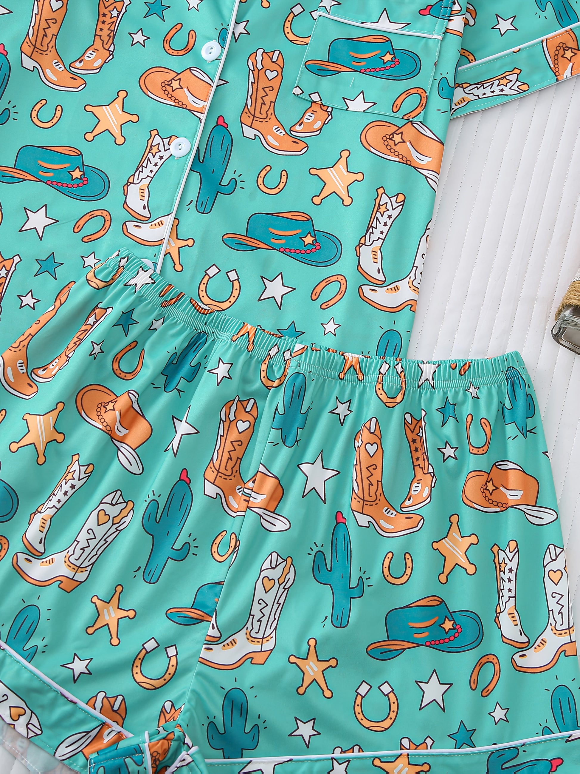 Turquoise satin-look pajama set with western boot and horseshoe print — short-sleeve button-up top with chest pocket and elastic waist shorts, 95% Polyester/5% Elastane