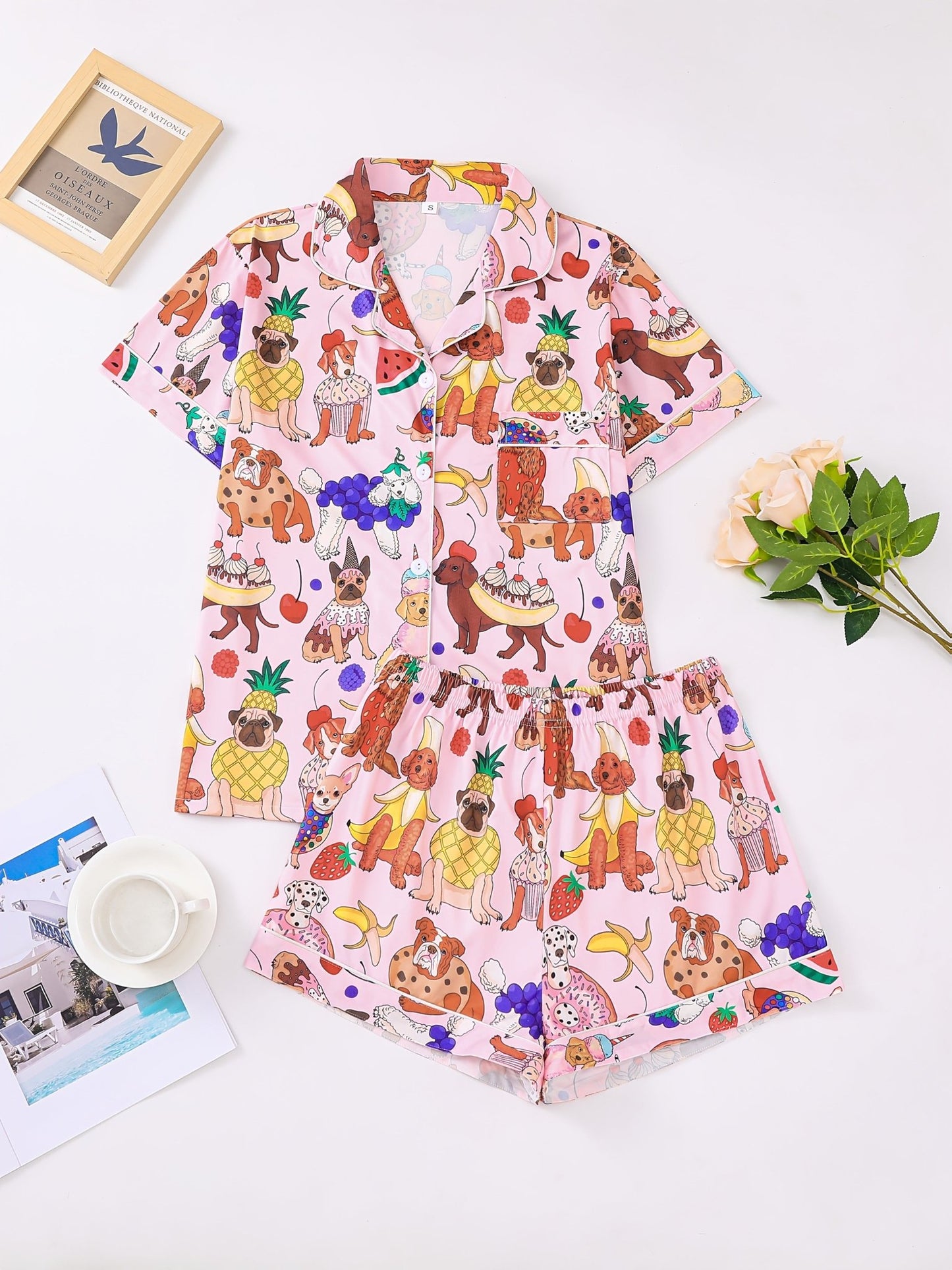 Pink satin-look short-sleeve pajama set with colorful puppy and fruit print, piped trim, chest pocket and elastic waist shorts in 95% Polyester 5% Elastane — silky stretch travel-ready loungewear