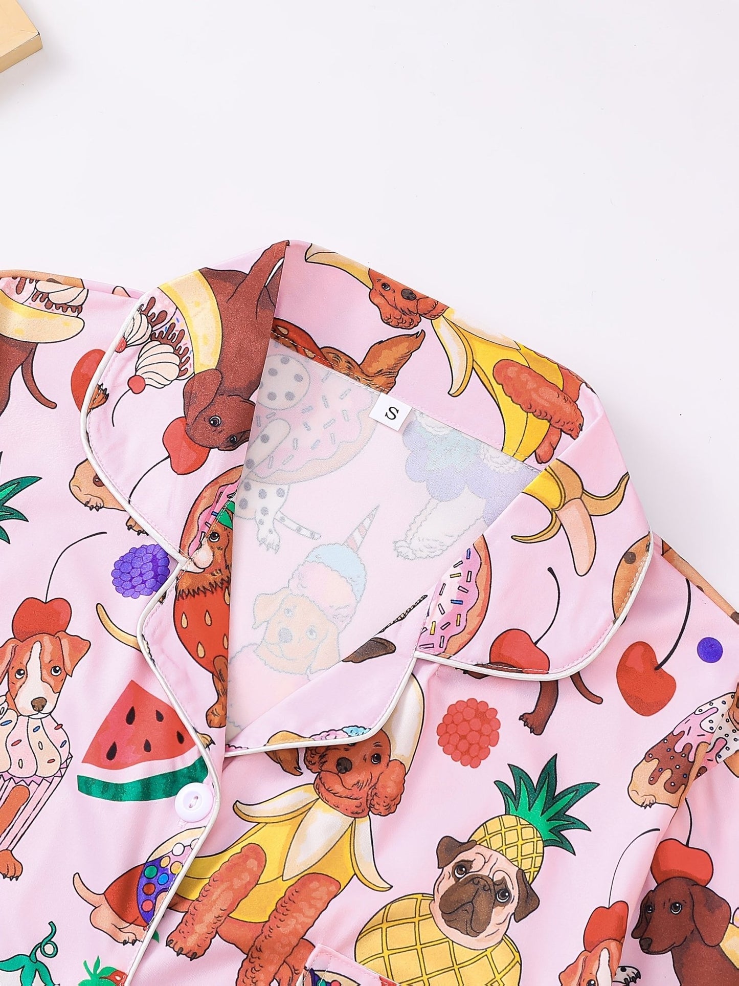 Pink satin-look short-sleeve pajama set with colorful puppy and fruit print, piped trim, chest pocket and elastic waist shorts in 95% Polyester 5% Elastane — silky stretch travel-ready loungewear