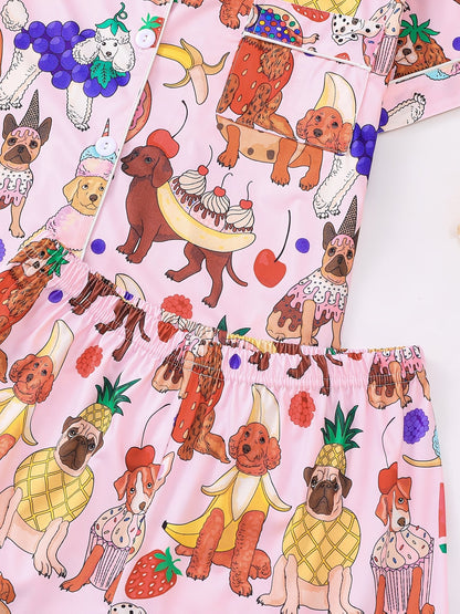 Pink satin-look short-sleeve pajama set with colorful puppy and fruit print, piped trim, chest pocket and elastic waist shorts in 95% Polyester 5% Elastane — silky stretch travel-ready loungewear