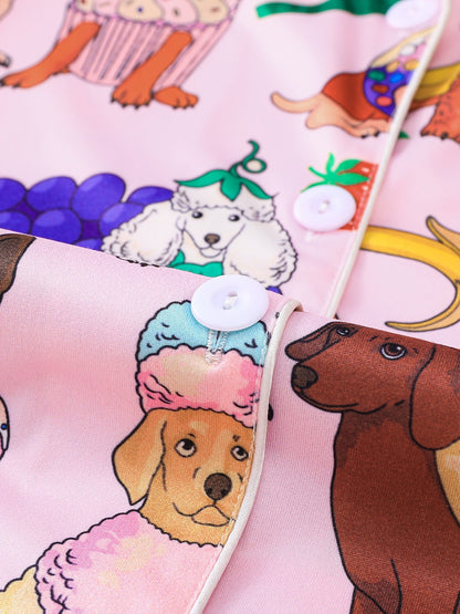 Pink satin-look short-sleeve pajama set with colorful puppy and fruit print, piped trim, chest pocket and elastic waist shorts in 95% Polyester 5% Elastane — silky stretch travel-ready loungewear