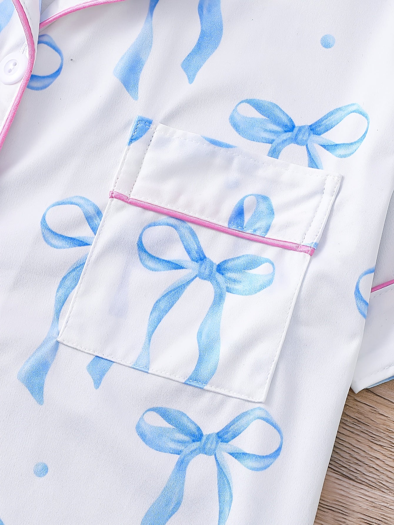 White satin-look pajama set with blue watercolor bow print, short-sleeve button top with piped pocket and elastic waist full-length pants — 95% Polyester/5% Elastane, silky and breathable