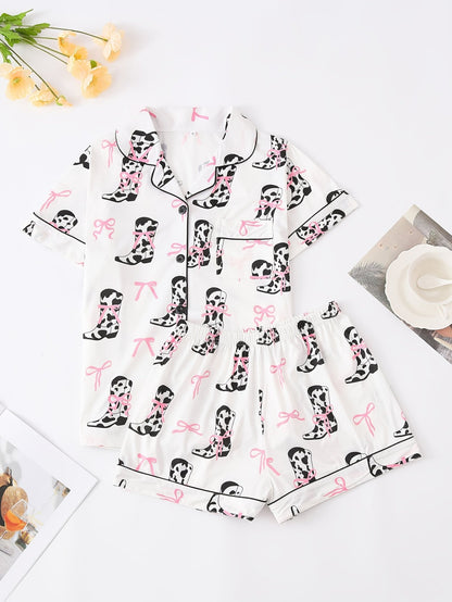 White cow-print short-sleeve pajama set with pink bow accents in silky 95% Polyester 5% Elastane, featuring chest pocket and elastic waist shorts
