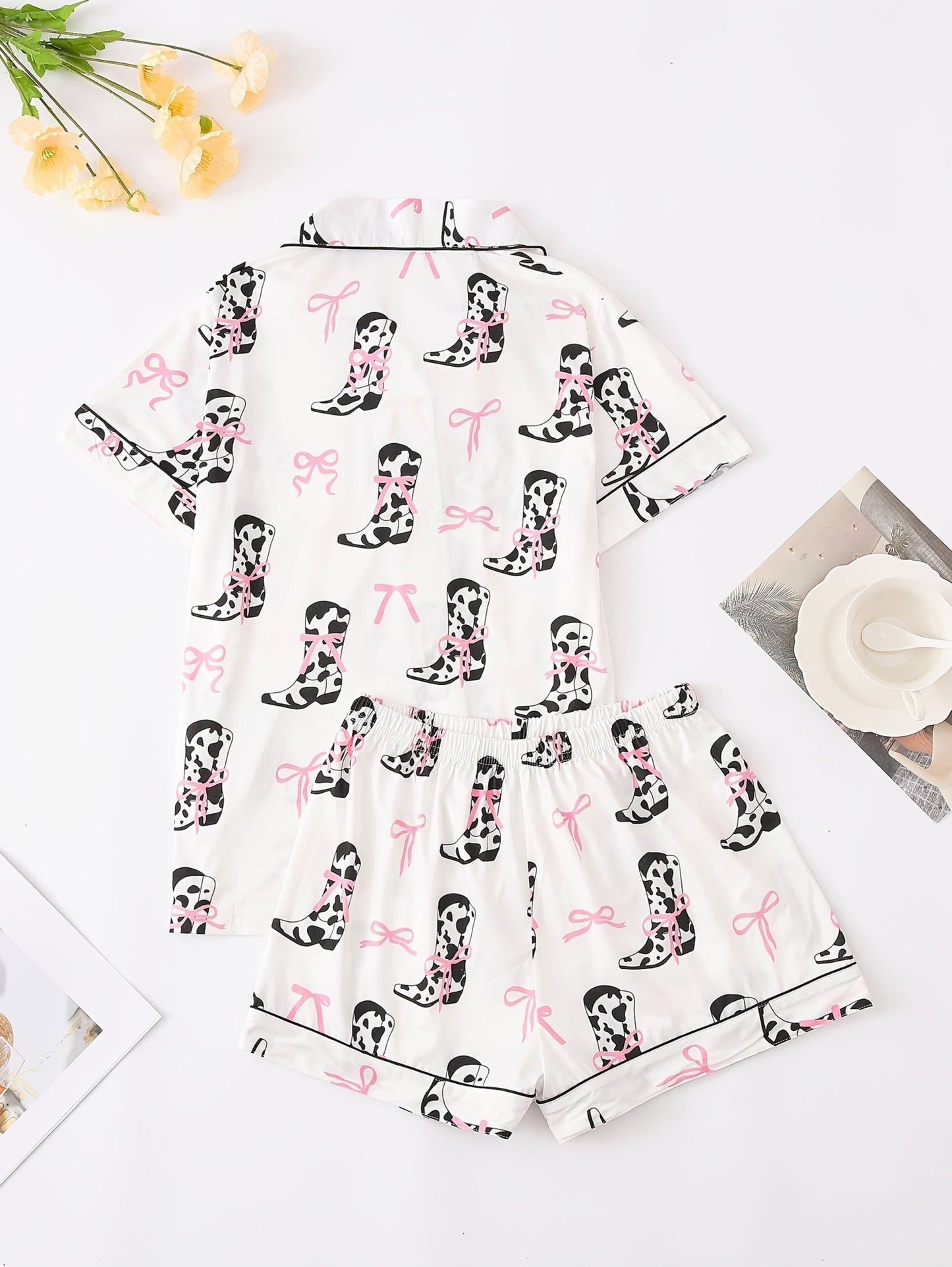 White cow-print short-sleeve pajama set with pink bow accents in silky 95% Polyester 5% Elastane, featuring chest pocket and elastic waist shorts