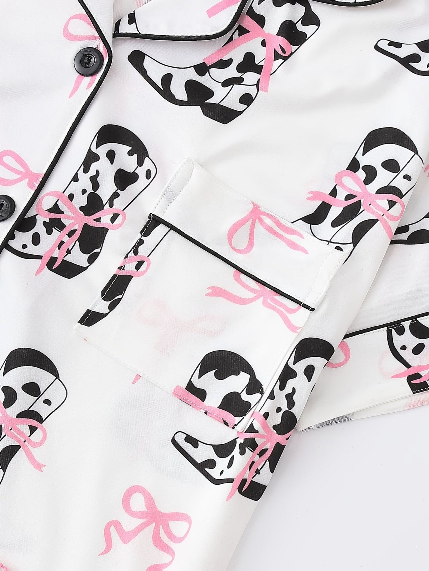 White cow-print short-sleeve pajama set with pink bow accents in silky 95% Polyester 5% Elastane, featuring chest pocket and elastic waist shorts