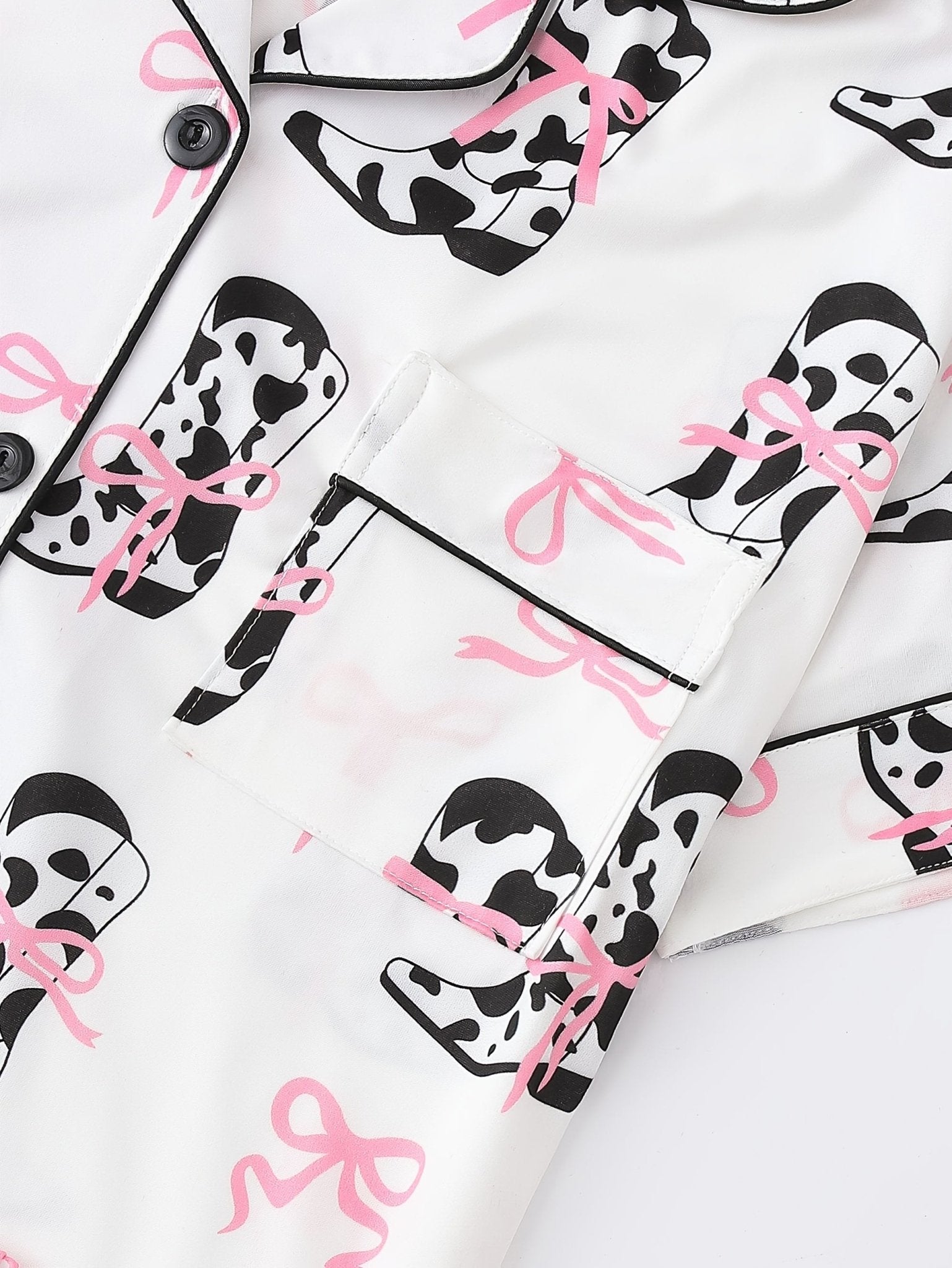 White cow-print short-sleeve pajama set with pink bow accents in silky 95% Polyester 5% Elastane, featuring chest pocket and elastic waist shorts
