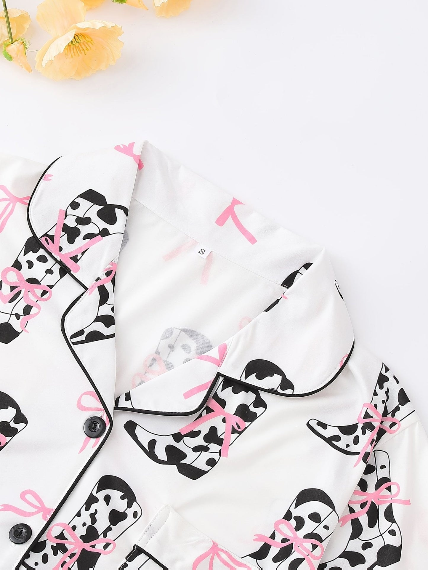 White cow-print short-sleeve pajama set with pink bow accents in silky 95% Polyester 5% Elastane, featuring chest pocket and elastic waist shorts