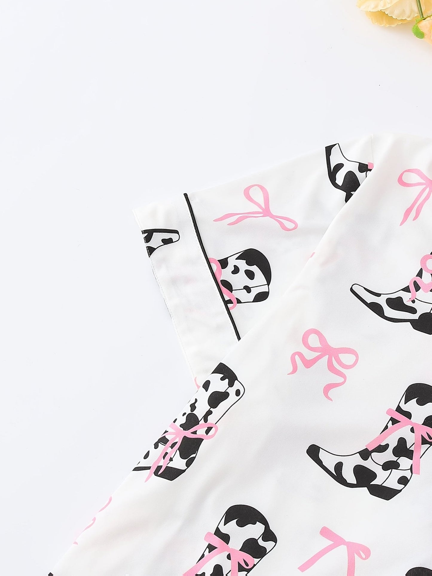 White cow-print short-sleeve pajama set with pink bow accents in silky 95% Polyester 5% Elastane, featuring chest pocket and elastic waist shorts