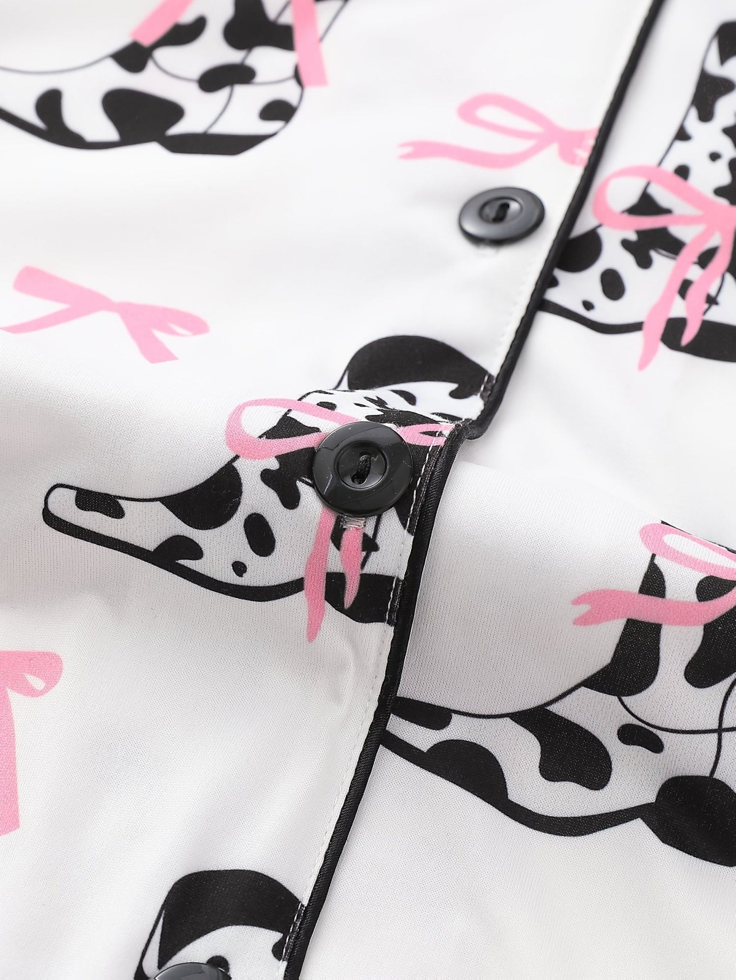 White cow-print short-sleeve pajama set with pink bow accents in silky 95% Polyester 5% Elastane, featuring chest pocket and elastic waist shorts
