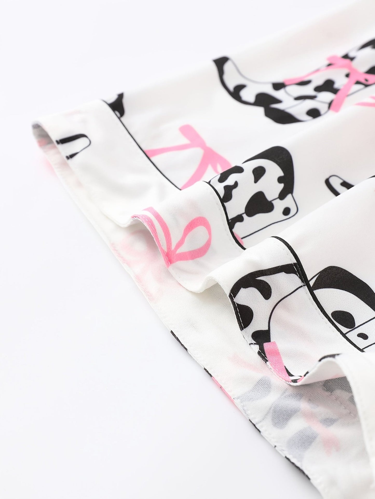 White cow-print short-sleeve pajama set with pink bow accents in silky 95% Polyester 5% Elastane, featuring chest pocket and elastic waist shorts