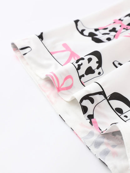 White cow-print short-sleeve pajama set with pink bow accents in silky 95% Polyester 5% Elastane, featuring chest pocket and elastic waist shorts